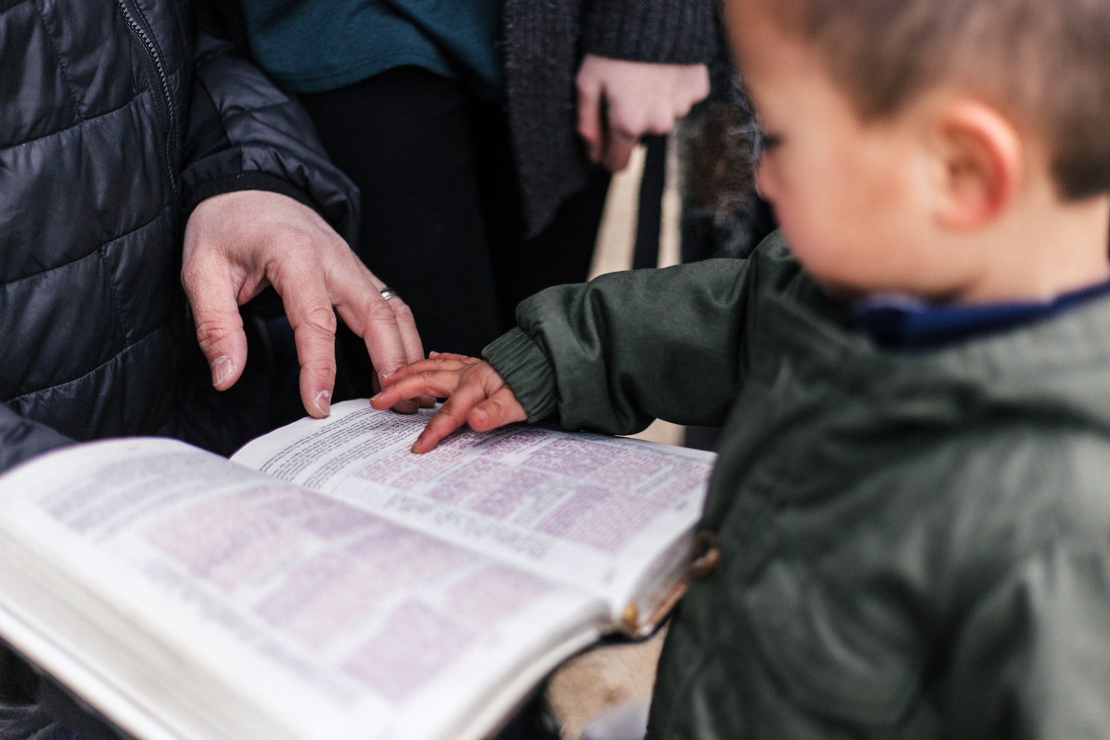 Small child touching and Bible as parent looks on